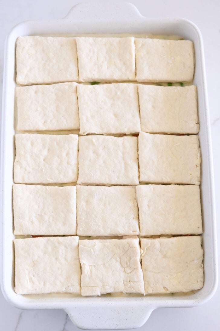 White 9X13-inch pan with chicken pot pie filling topped with unbaked square biscuits.