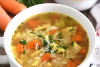 Chicken and rice soup in white bowl with handles topped with fresh parsley and Parmesan cheese.