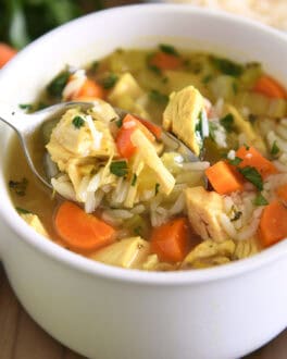 Spoon lifting up scoop of chicken and rice soup in white bowl with handles topped with fresh parsley and Parmesan cheese.