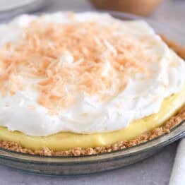Whole coconut cream pie in glass pie plate topped with whipped cream and toasted coconut.