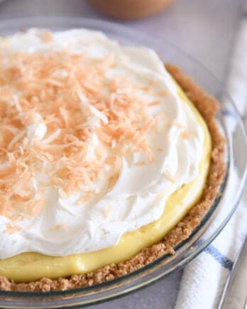 Whole coconut cream pie in glass pie plate topped with whipped cream and toasted coconut.