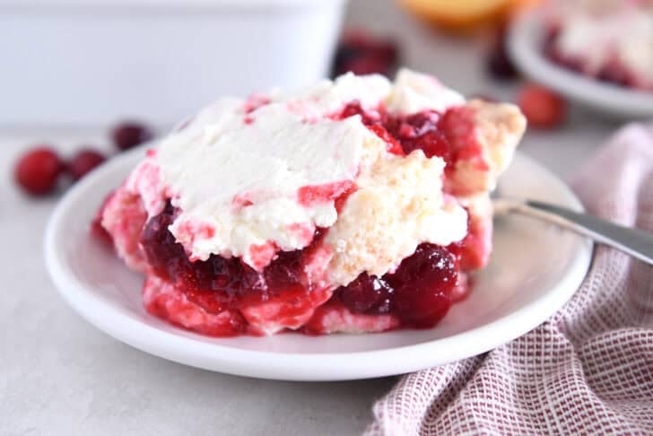 Scoop of cranberry orange layered angel food cake dessert on white plate with spoon.