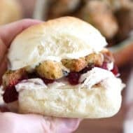 Holding homemade roll sandwiched with mayonnaise, stuffing, cranberry sauce and shredded turkey between fingers.