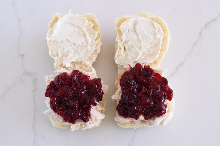 Two rolls open, spread with mayo, and shredded turkey and cranberry sauce on bottom halves.