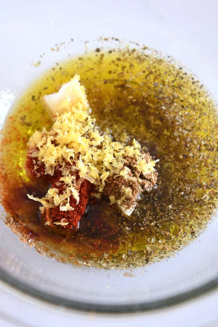 Top down view of a glass bowls with oil, seasonings, and lemon zest.