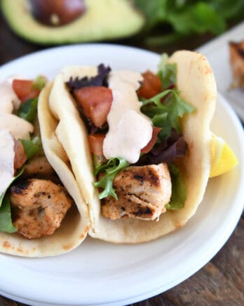 Flatbread grilled chicken wraps with lettuce, tomatoes, and creamy sauce on a white plate.