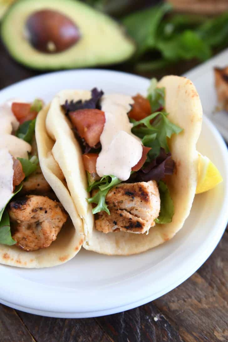 Flatbread grilled chicken wraps with lettuce, tomatoes, and creamy sauce on a white plate.