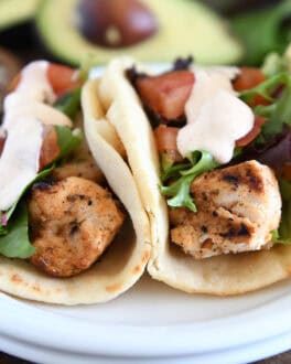 Flatbread grilled chicken wraps with lettuce, tomatoes, and creamy sauce on a white plate.