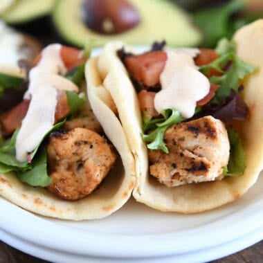 Flatbread grilled chicken wraps with lettuce, tomatoes, and creamy sauce on a white plate.