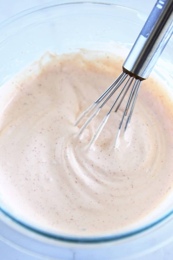 Top down view of a glass bowl with a creamy white sauce and a wire whisk.