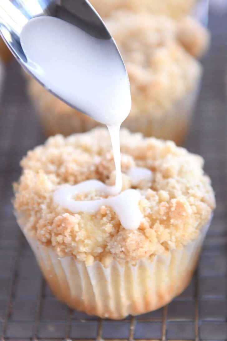 A spoon drizzling white glaze on a lemon crumb muffin.