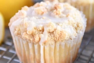 Lemon muffins with a crumb topping and white glaze on a cooling rack.