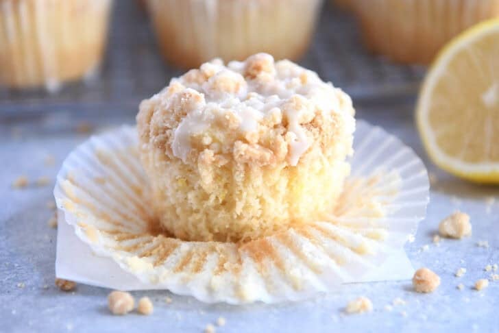 A lemon muffin topped with a crumb topping and white glaze sitting on a muffin liner.