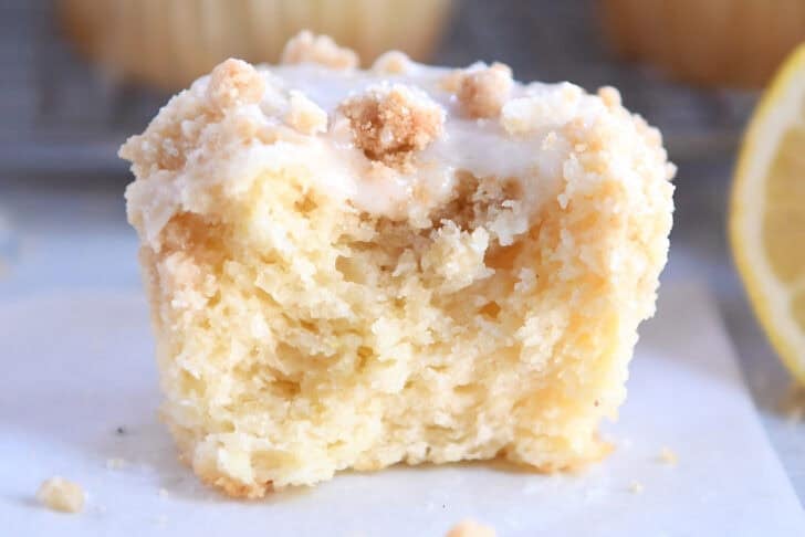 A half eaten lemon muffin with a crumb topping and white glaze.