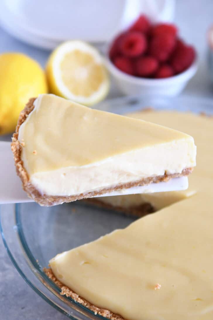 A spatula taking a slice of graham-cracker crust lemon pie out of a full lemon pie.