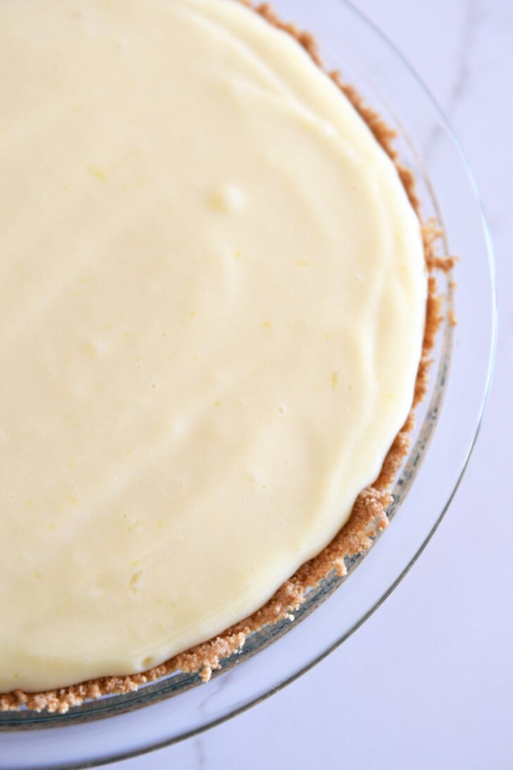 Top down view showing half of a lemon pie with a graham cracker crust in a glass pie dish.