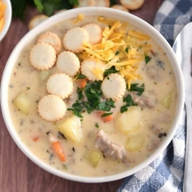 Soup bowl with sausage potato soup topped with oyster saltine crackers, fresh parsley and grated cheese.