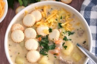 Soup bowl with sausage potato soup topped with oyster saltine crackers, fresh parsley and grated cheese and spoon on side.