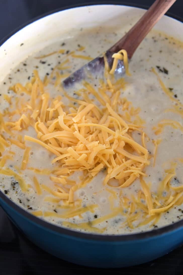 Freshly grated cheddar cheese in soup pot with creamy soup.