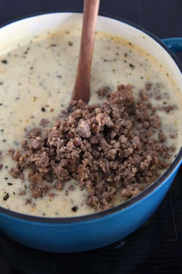 Cooked, crumbled sausage in soup pot with creamy soup.