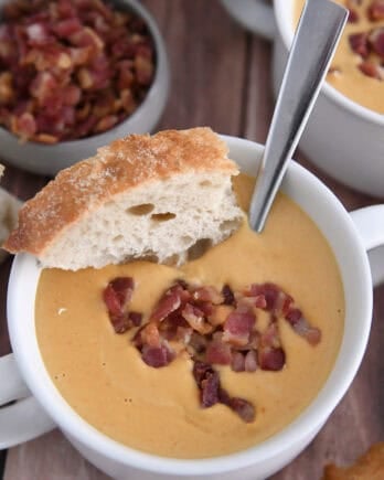 Top down view of butternut squash soup in white bowl topped with bacon and piece of crusty bread.