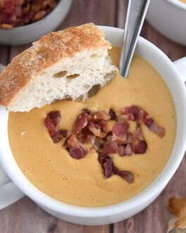 Top down view of butternut squash soup in white bowl with piece of crusty bread and cooked bacon pieces.