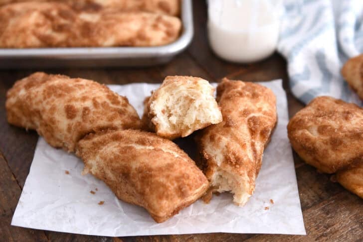 Three cinnamon sugar twists on white parchment paper with one broken in half.