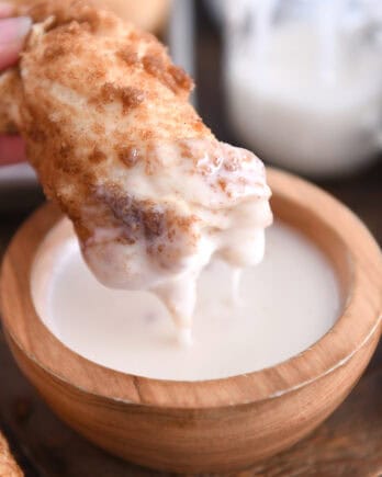 Dipping cinnamon sugar twist in bowl of sweet icing.