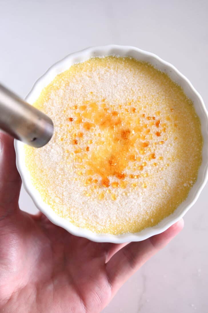 Using kitchen torch to caramelize the top of creme brulee in white ramekin.