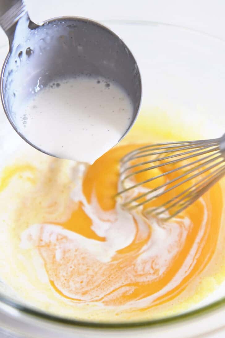Tempering egg yolks and sugar by drizzling hot cream off a ladle into glass bowl with whisk.