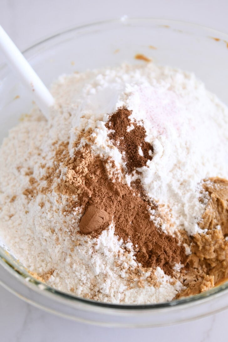 Glass bowl with cookie batter, flour, cinnamon, salt, and allspice.