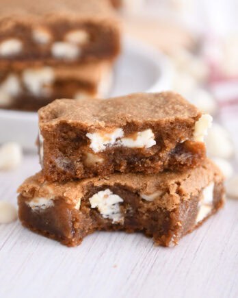Two squares of white chocolate gingerbread blondie bars stacked with bite taken out of bottom bar.