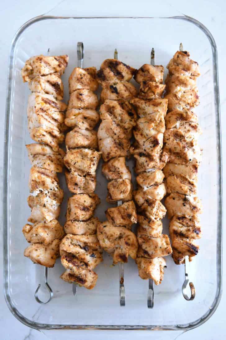 Top down view of a glass dish filled with grilled chicken kebabs.