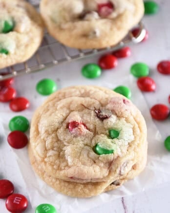 Two baked chocolate chip cookies with red and green M&Ms stacked on parchment paper.