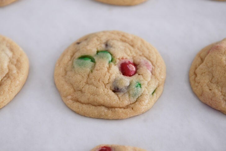 Baked cookies with red and green M&Ms on parchment paper.