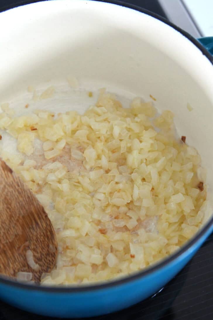 Cast iron enamel pot with cooked onions in butter.
