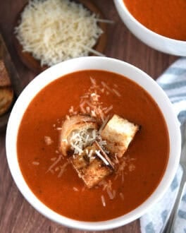 Top down view of white bowl filled with homemade tomato soup, homemade croutons and parmesan cheese.
