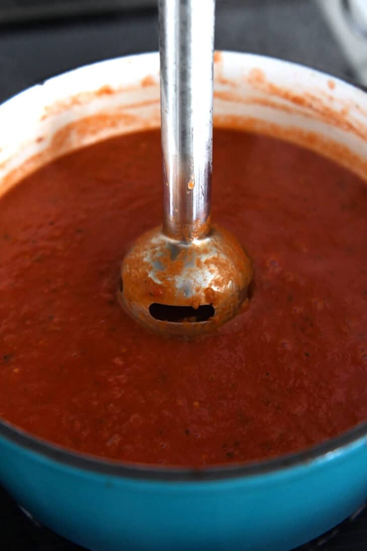 Immersion blender in cast iron enamel pot of tomato soup.