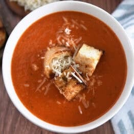 Top down view of white bowl filled with homemade tomato soup, homemade croutons and parmesan cheese.