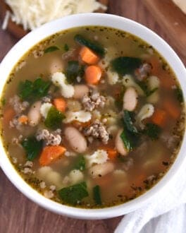 Top down photo of white bowl with broth, carrots, white beans, small pasta, and spinach.