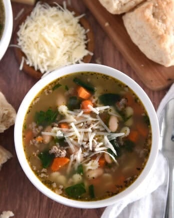 Top down photo of white bowl with broth, carrots, white beans, small pasta, spinach and Parmesan cheese.