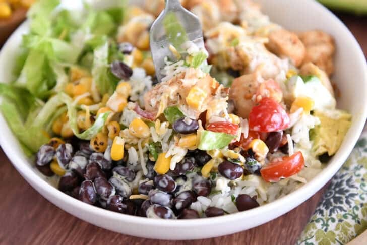 White bowl with fork scooping up cilantro lime rice, black beans, corn, chicken, and dressing.