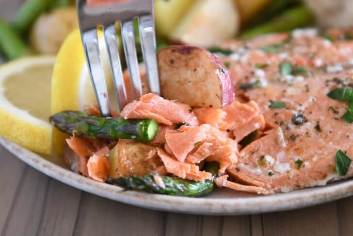 Gray plate with fork, pieces of baked salmon, asparagus and roasted potatoes.
