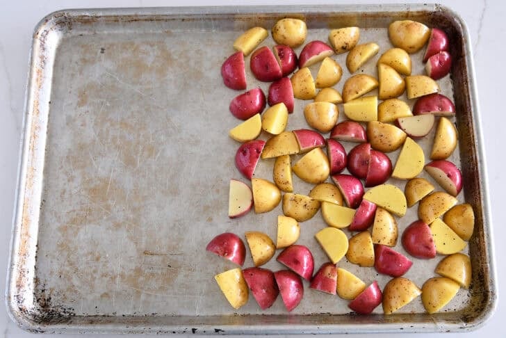Top down view of sheet pan with cut red and yellow potatoes.