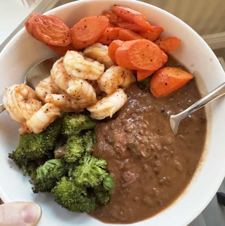 White bowl with lentil soup, broccoli, shrimp and carrots.