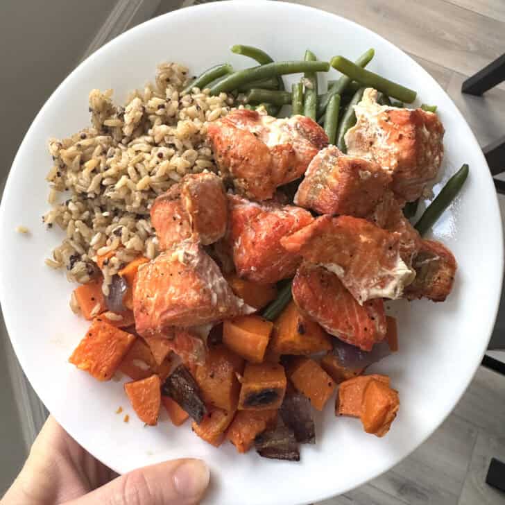 White plate with brown rice, sweet potatoes, green beans and salmon bites.