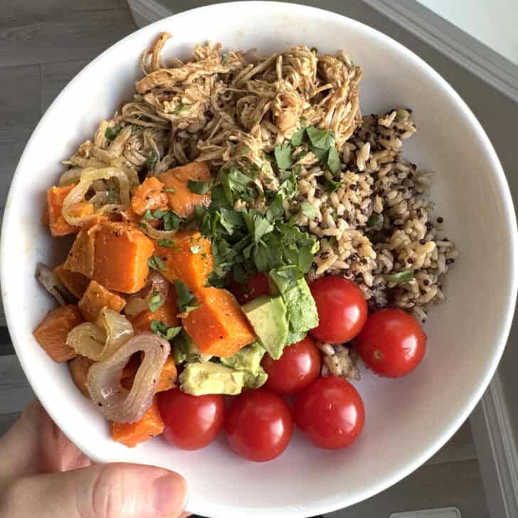 White plate with sweet potatoes, onions, avocados, cherry tomatoes, brown rice and salsa verde chicken.
