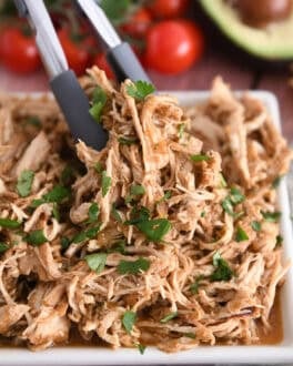 Tongs grabbing portion of salsa verde chicken on white tray.