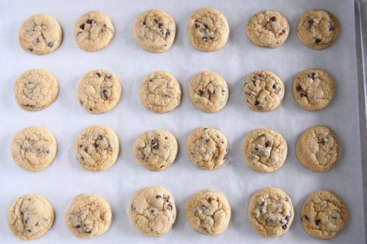 Top down view of 24 mini chocolate chip cookies on a parchment-lined baking sheet.