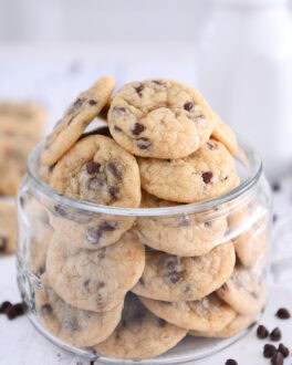 Glass jar filled with mini chocolate chip cookies with mini chocolate chips around bottom.